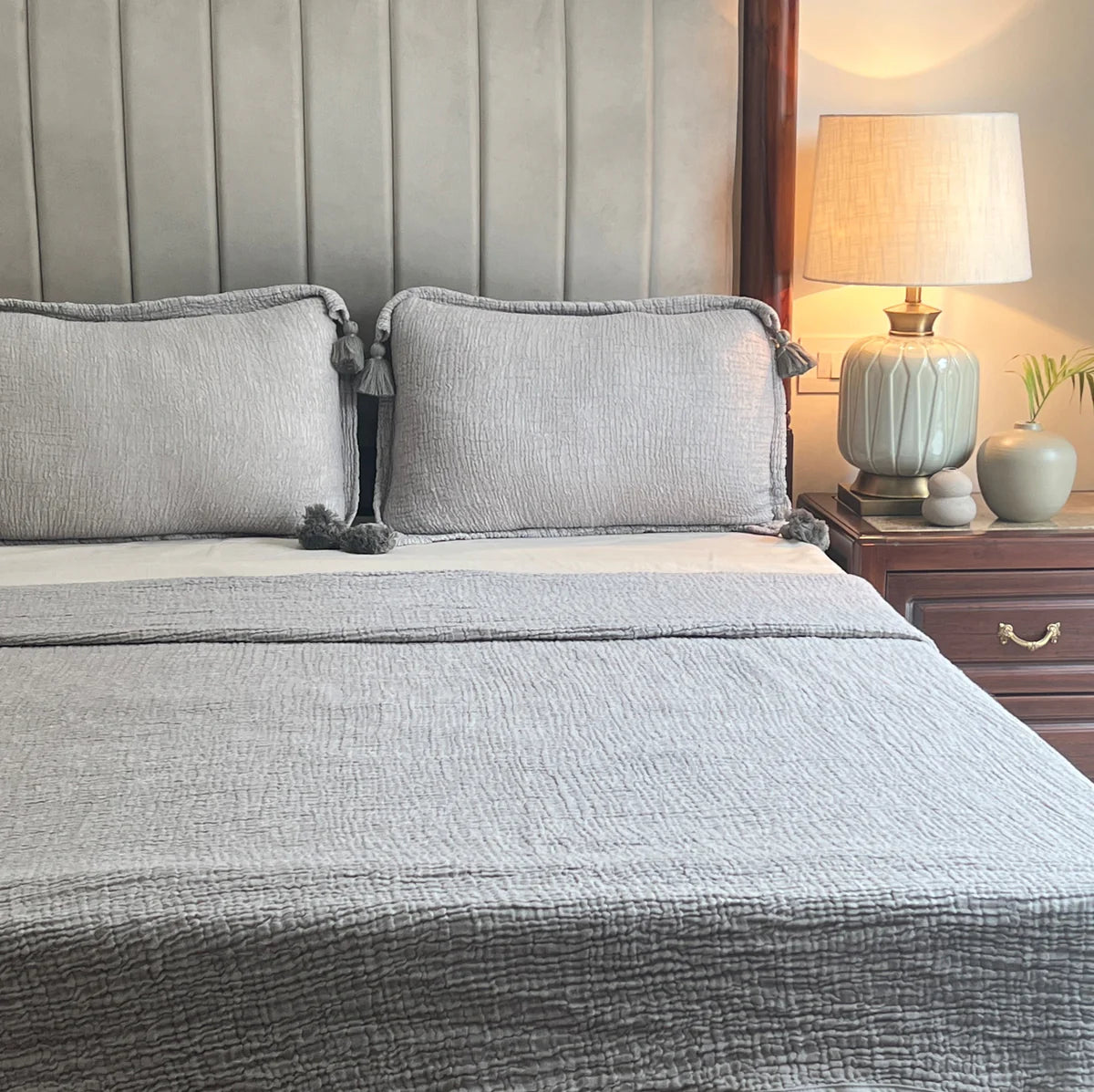 Slate grey woven bedspread with matching pillow shams and tassel detail.