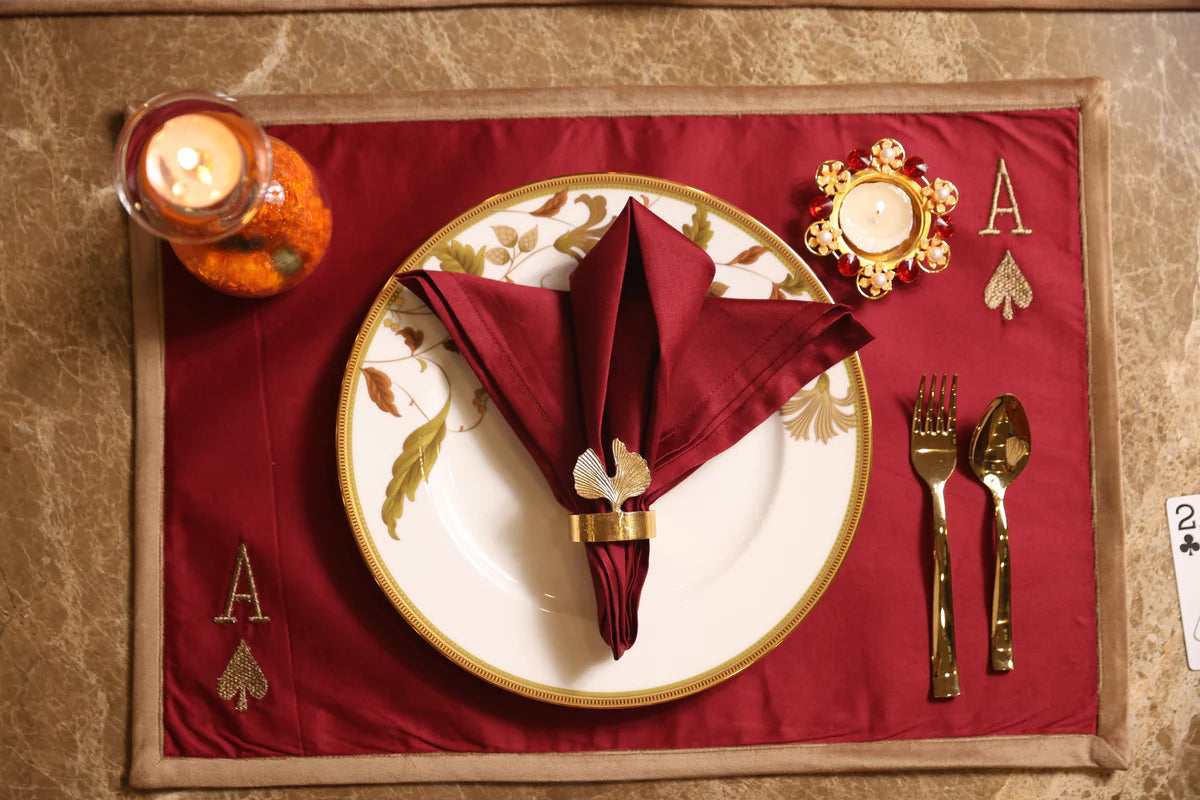 Burgundy embroidered table linen set with gold cutlery and napkin ring.
